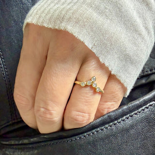 Karen Karch 18k yellow gold tiara ring featuring bezel-set round diamonds arranged to create a "v" shape. This configuration is crowned with an outward pointing pear-shape bezel. Shown on a hand.