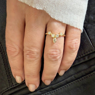 Karen Karch 18k yellow gold tiara ring featuring bezel-set round diamonds arranged to create a "v" shape. This configuration is crowned with an outward pointing pear-shape bezel. Shown on a hand.