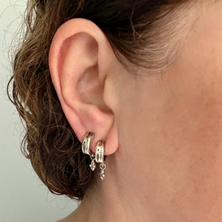 Close-up of an ear with two Karen Karch Jaipur Mainstay silver hoop earrings with small metal drops.