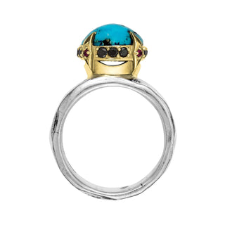 Top view of a Karen Karch weathered silver wide band ring featuring a large round turquoise cabochon raised up in a gold claw setting, studded with Black Diamonds and Rubies around the base shown against a plain white background.