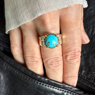 Karen Karch King of Rings Mixed Metal gold setting amd a wide silver band with a large round matrix tuquoise cabochon on a hand.