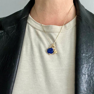 Karen Karch Reminiscent Rose gold rosebud charm with a twining vine that forms a loop ending in a ruby layered on a chain with a carved lapis rosebud charm on a chain on a person