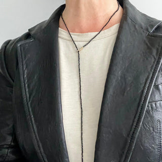 A person in a leather jacket wearing a black spinel gold lariat necklace with a weathered texture closure, featuring a loop and a pull-through bar-2