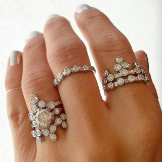 Karen Karch Turned Out Belgian Tiara Ring in Platinum with 10 diamonds in a crown like formation stacked on pointer finger with other platinum diamond rings on a hand.