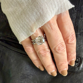 Karen Karch ring with two textured sterling silver bands intertwine with delicate vine details and four bezel-set black diamonds flanking an 11mm round center rutilated quartz in a claw setting on a hand. 