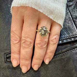 Karen Karch 18k Yellow Gold Dark Grey Oval Diamond ring surrounded by a order of black and white diamonds. There are 3 diamonds each side of center on the band. shown on a hand.