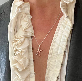 Karen Karch textured 10k rose gold charm in the shape of the letter 'K' with a vine-detail and rectangular bail on chain on a person.