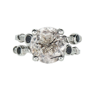 Front view of a Karen Karch ring with two textured sterling silver bands intertwine with delicate vine details and four bezel-set black diamonds flanking an 11mm round center rutilated quartz in a claw setting.