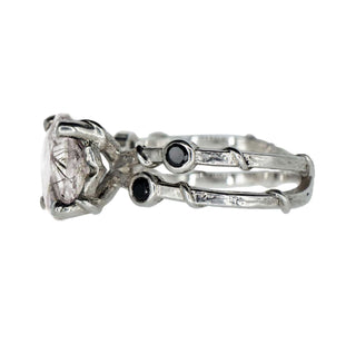 Side view of a Karen Karch ring with two textured sterling silver bands intertwine with delicate vine details and four bezel-set black diamonds flanking an 11mm round center rutilated quartz in a claw setting.