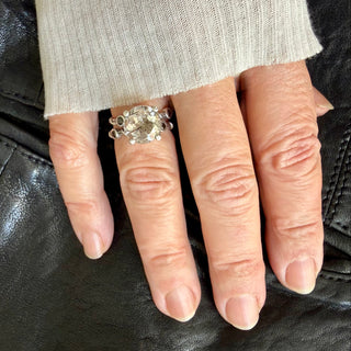 Karen Karch ring with two textured sterling silver bands intertwine with delicate vine details and four bezel-set black diamonds flanking an 11mm round center rutilated quartz in a claw setting on a hand. 