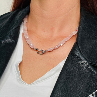 Close-up of a person wearing a Karen  Karch by Deme Wolfe rose quartz faceted rectangular beaded necklace with a silver snake clasp set with 2 black spinel square gems.