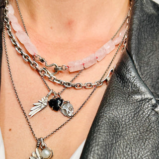Karen Karch by Deme Wolfe Silver Skull pendant with raised silver shapes and a mini crown layered with various other charms beads and chains on a person.