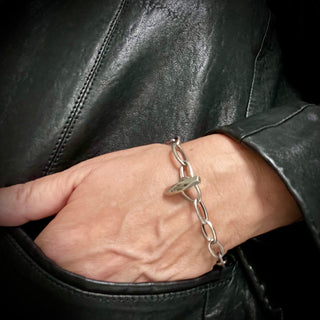 A person's wrist wearing a Karen Karch Outshine Toggle silver bracelet with an oval link chain design, held against a backdrop of black leather.