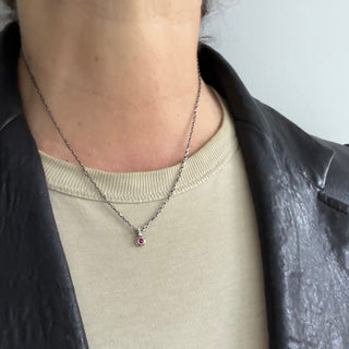 Karen Karch Silver Charm Necklace with a small round red ruby gemstone pendant on a thin chain on a neck.