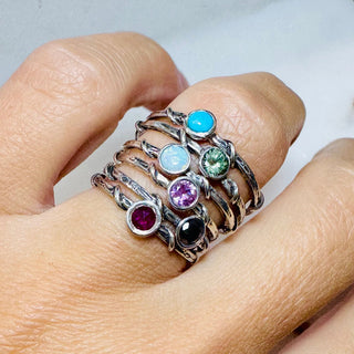 Karen Karch Silver Vine Stacker Rings stacked on a finger with bezel-set color gems and a black diamond. 