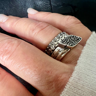 Karen Karch silver Signet Wrap ring studded with black diamonds stacked with other silver rings on a hand.
