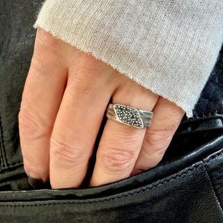 Hand wearing a Karen Karch silver Signet Wrap ring studded with black diamonds, partially inserted into a black leather pocket.