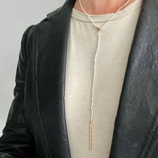 A person wearing a leather jacket wearing a white rice pearl and 10k yellow gold  lariat with a weathered texture closure by Karen Karch