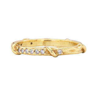 A weathered band in 18k yellow gold is detailed with organic twining vines is studded with colorless brilliant cut diamonds on the top half, side view, shown on a white background.
