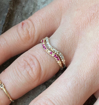 A Karen Karch by Deme Wolfe 14k yellow gold ring with rubies on the front of a curved band stacked with a similar band with diamonds on a finger. 