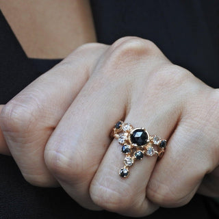 A Karen Karch 18k Rose Gold cocktail ring featuring a round rose cut black diamond center stone surrounded by smaller colorless and black diamonds, in a star-like formation on a hand.