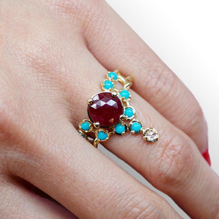Karen Karch Floating Star yellow gold ring featuring an 8mm rose cut ruby center surrounded by 2.3mm cabochon turquoise, and a diamond in a tiara ring on a hand